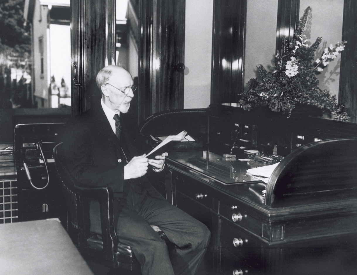 President George Albert Smith sitting at a desk in his office, reading a book.