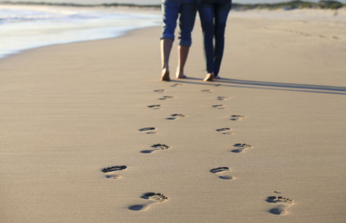 Couple Walking Across Beach Shoreline Leaving Footprints