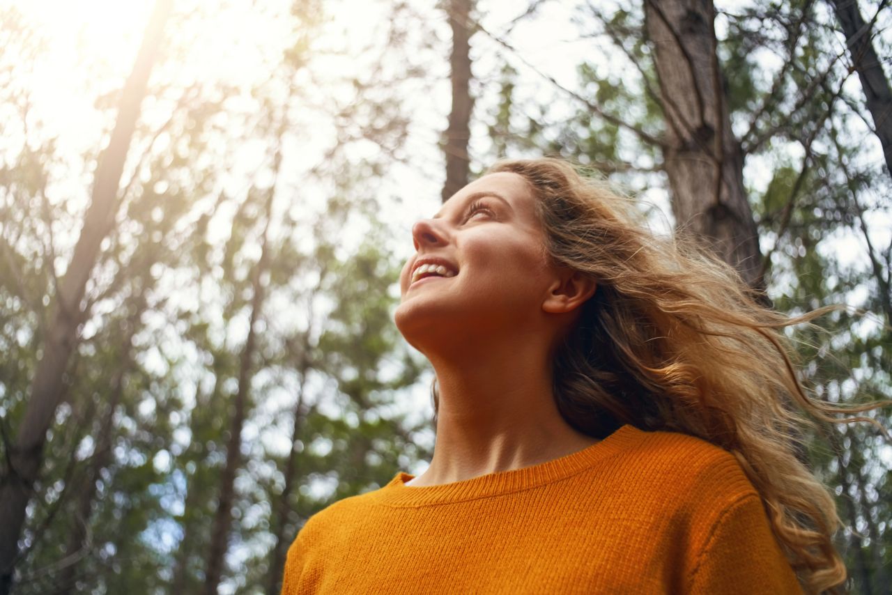 A young woman smiling enjoys time in the sunshine of a forest