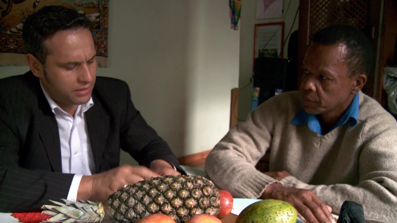 Two men sit a table with fruit