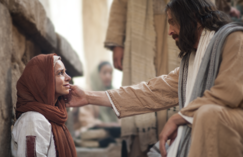 Jesus is touching the cheek of a woman who is sitting on the ground.  Outtakes include the ill woman walking up to Jesus to touch his clothes and Jesus kneeling and talking to the seated woman. 

Jesus touching the face of a seated woman.
