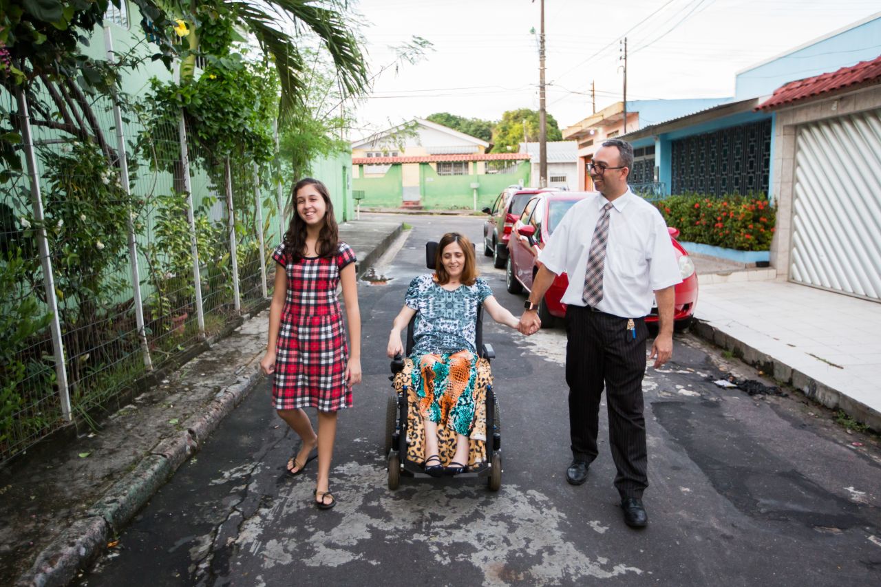 Uma esposa em uma cadeira de rodas é ajudada por seu marido e sua filha