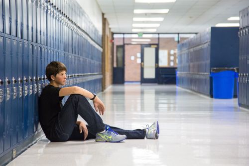 Young man sitting on floor, leaning against blue lockers in school hallway