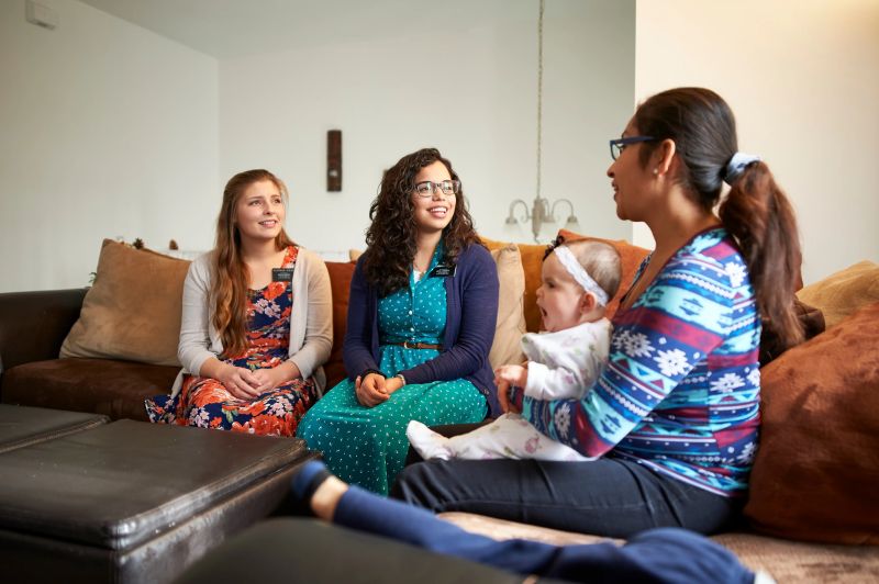 Duas missionárias ensinam uma jovem mãe e seu filho na sala de estar