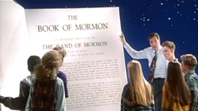 A group of students and their teacher examine a very large copy of the Book of Mormon