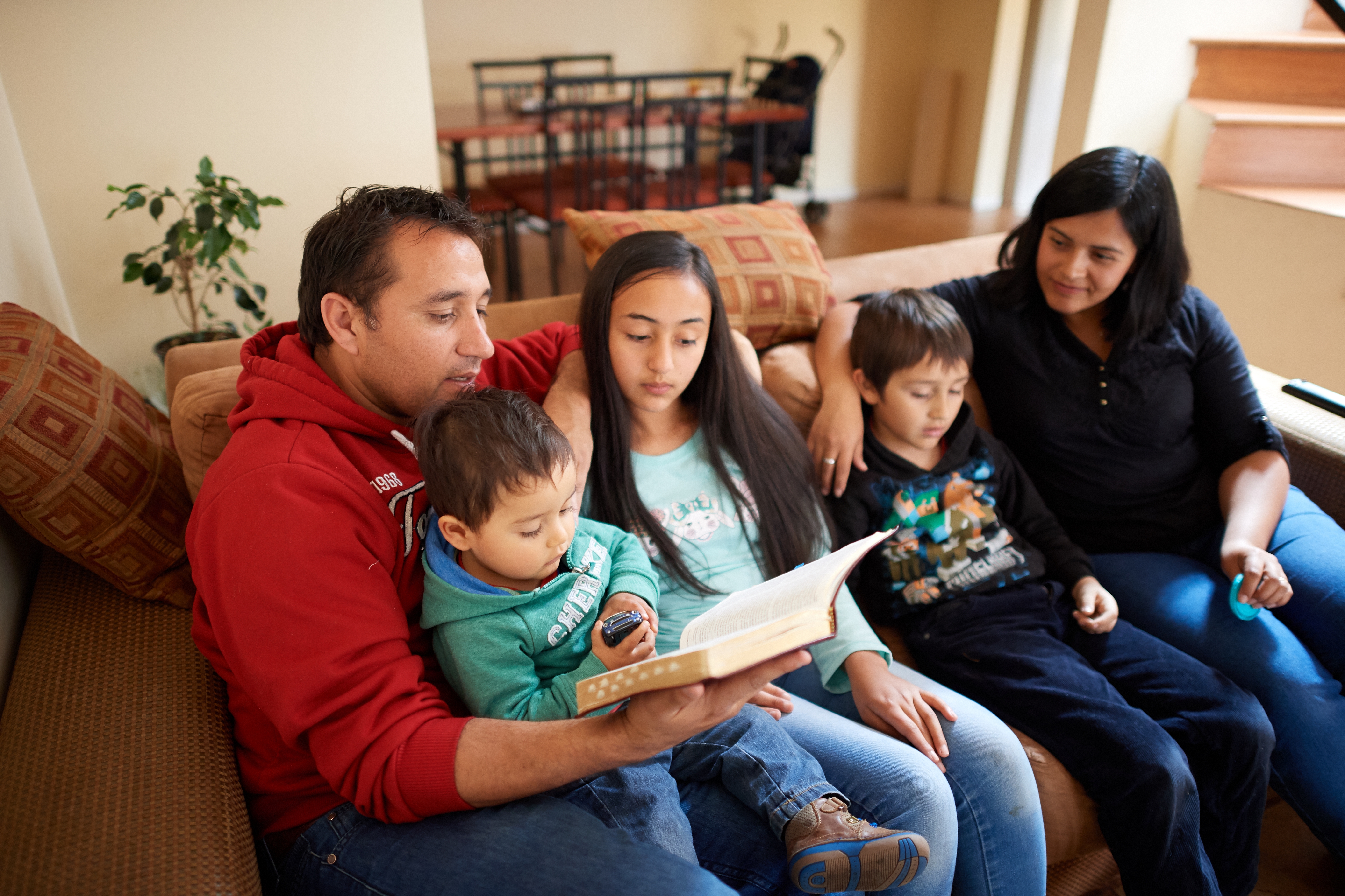 A family sits together on a couch and reads the scriptures together.