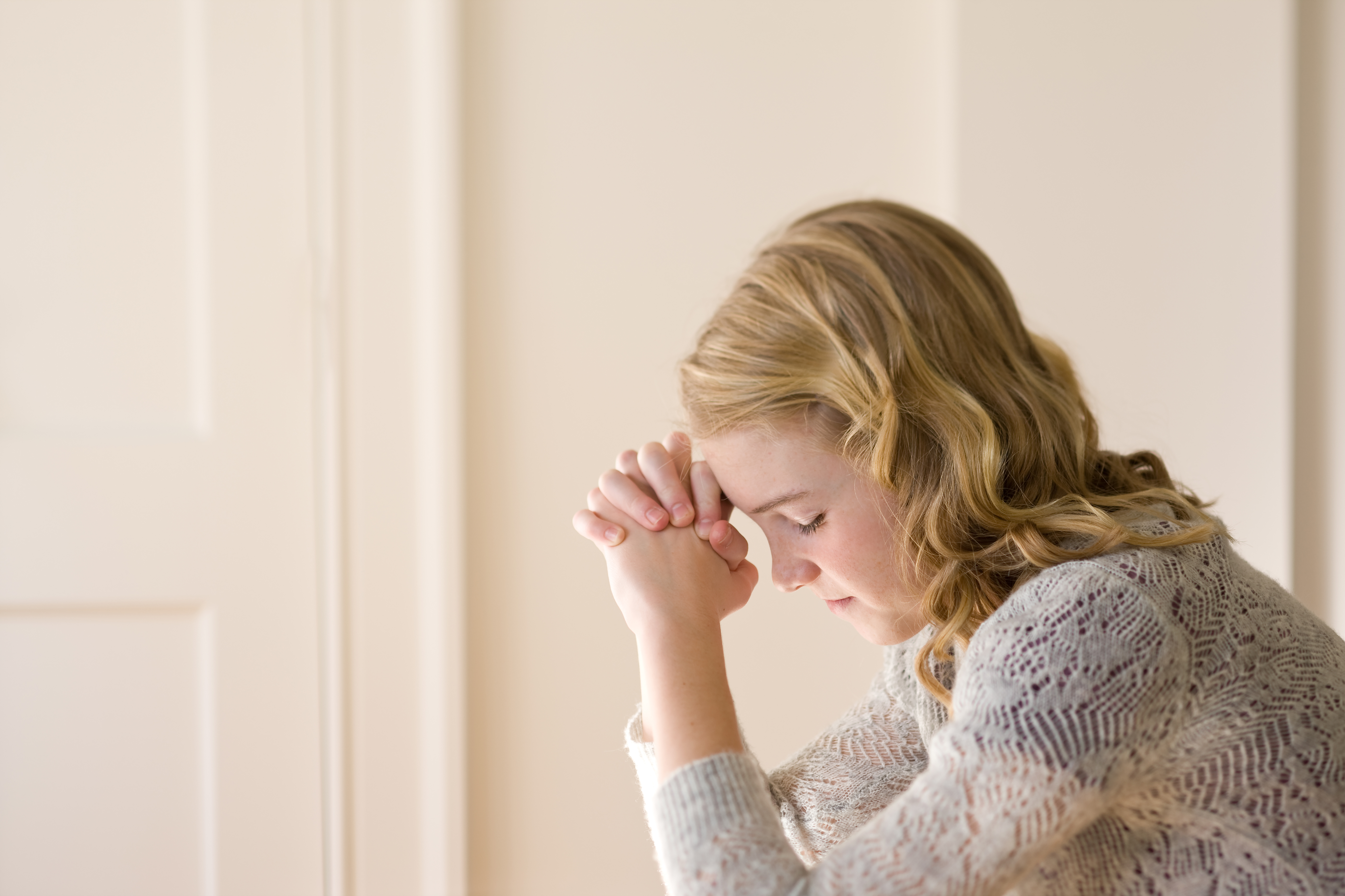 A young woman clasps her hands and rests her forehead on them, closes her eyes, and prays.