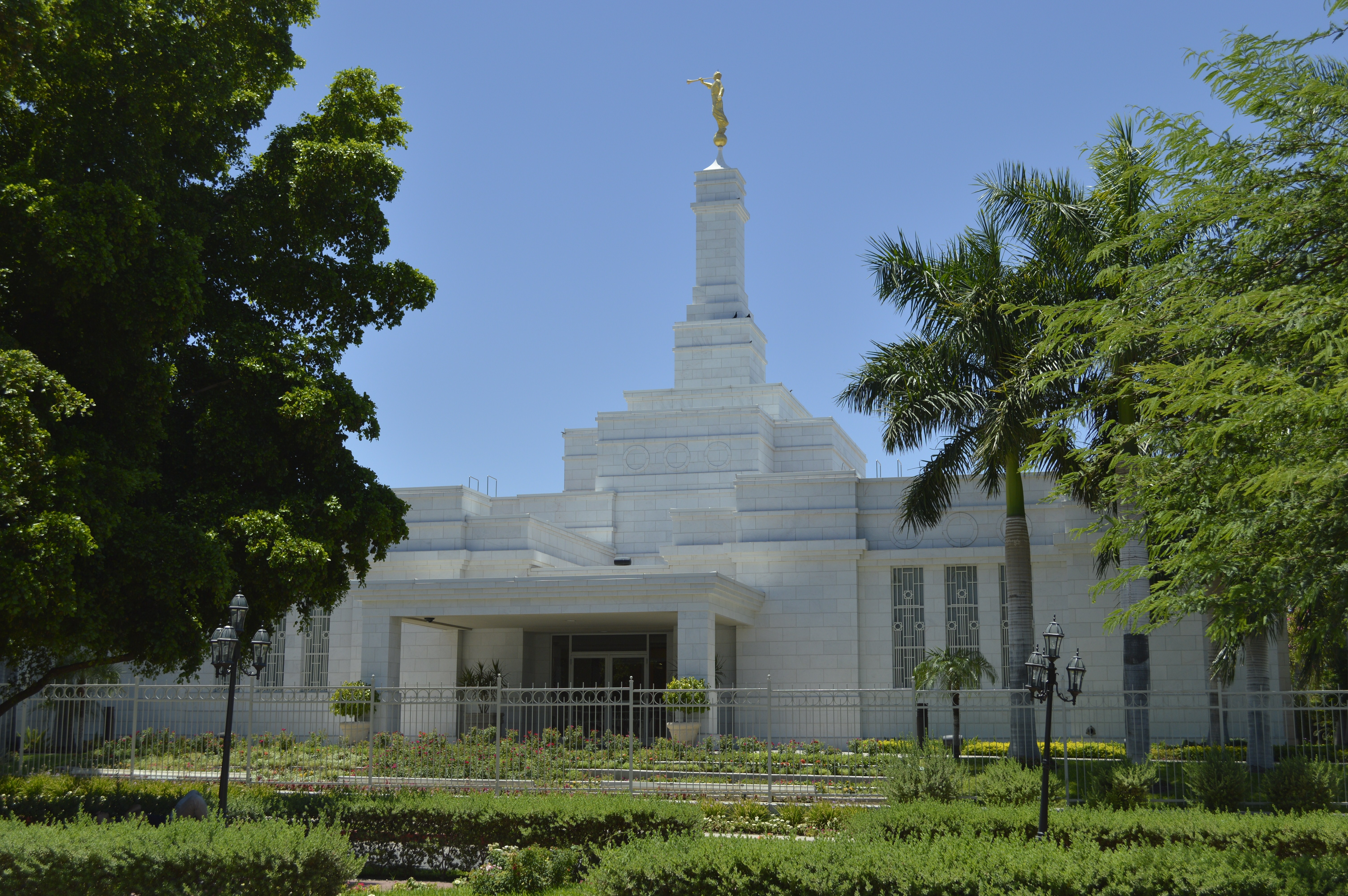 The Hermosillo Sonora Mexico Temple on a sunny day, surrounded by green shrubbery and trees.