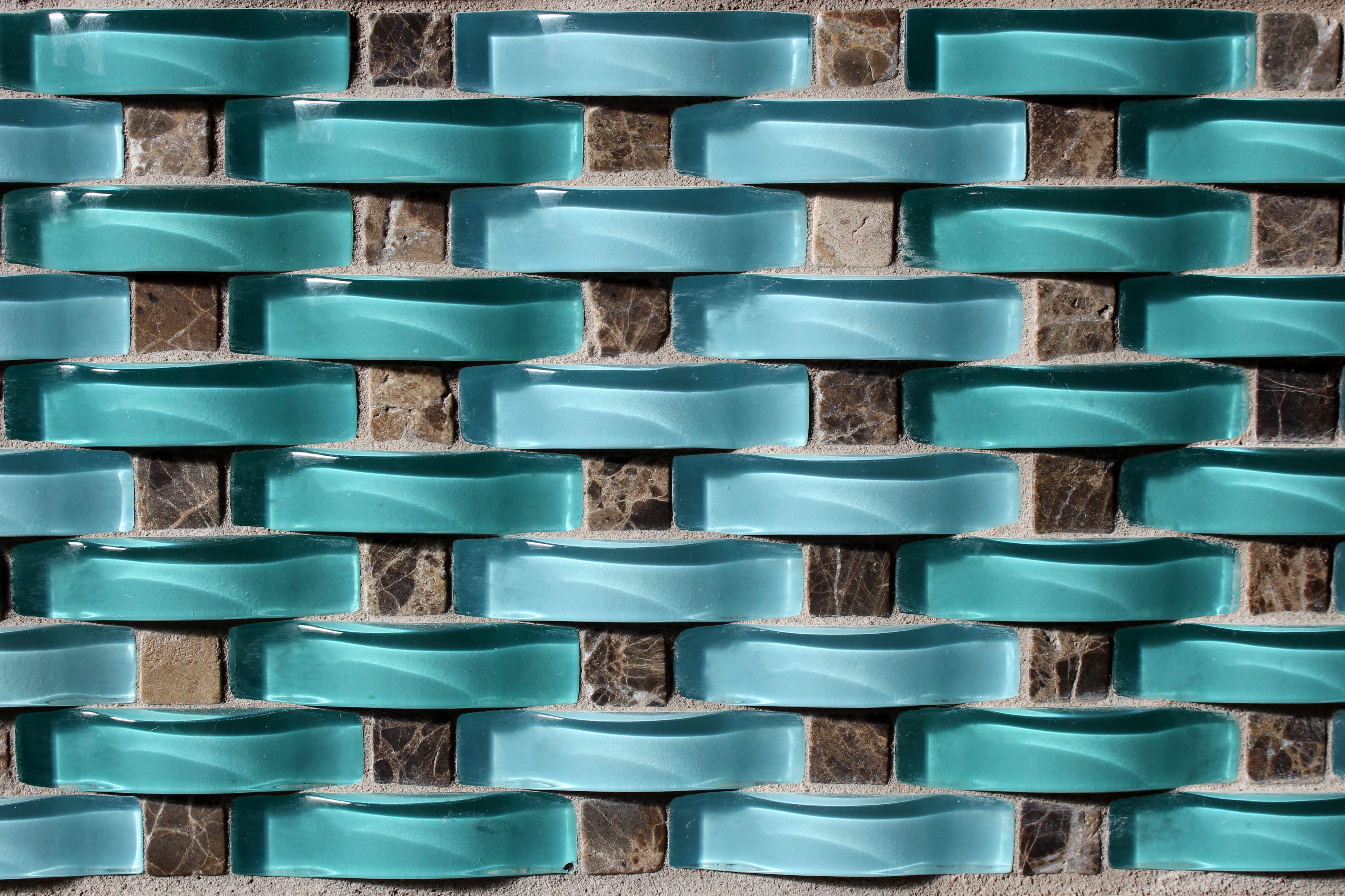 Curved sections of aqua-colored glass set between gray squares of tile-like cement.