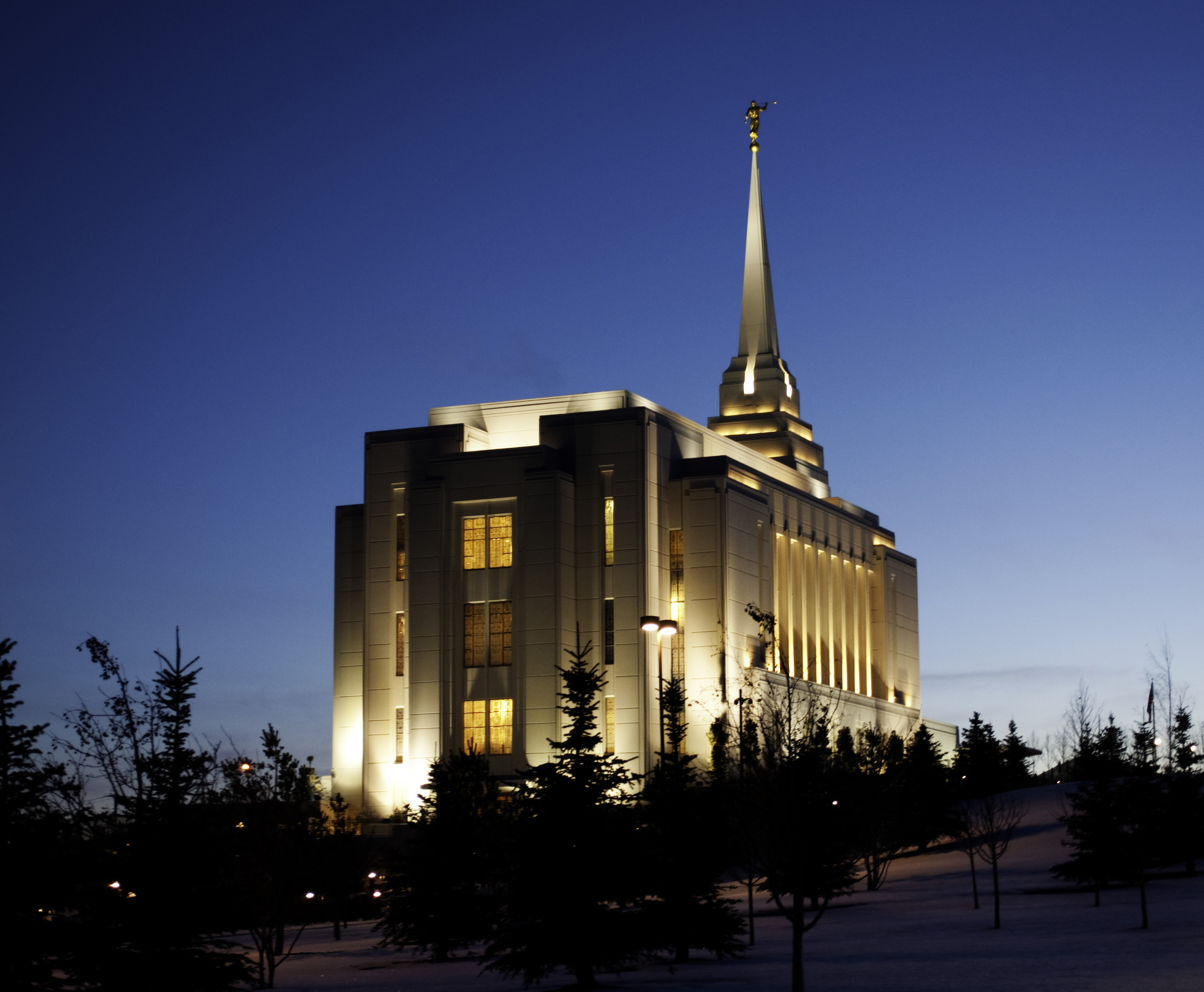 The back of the Rexburg Idaho Temple lit up at night, with a view of the trees on the temple grounds.