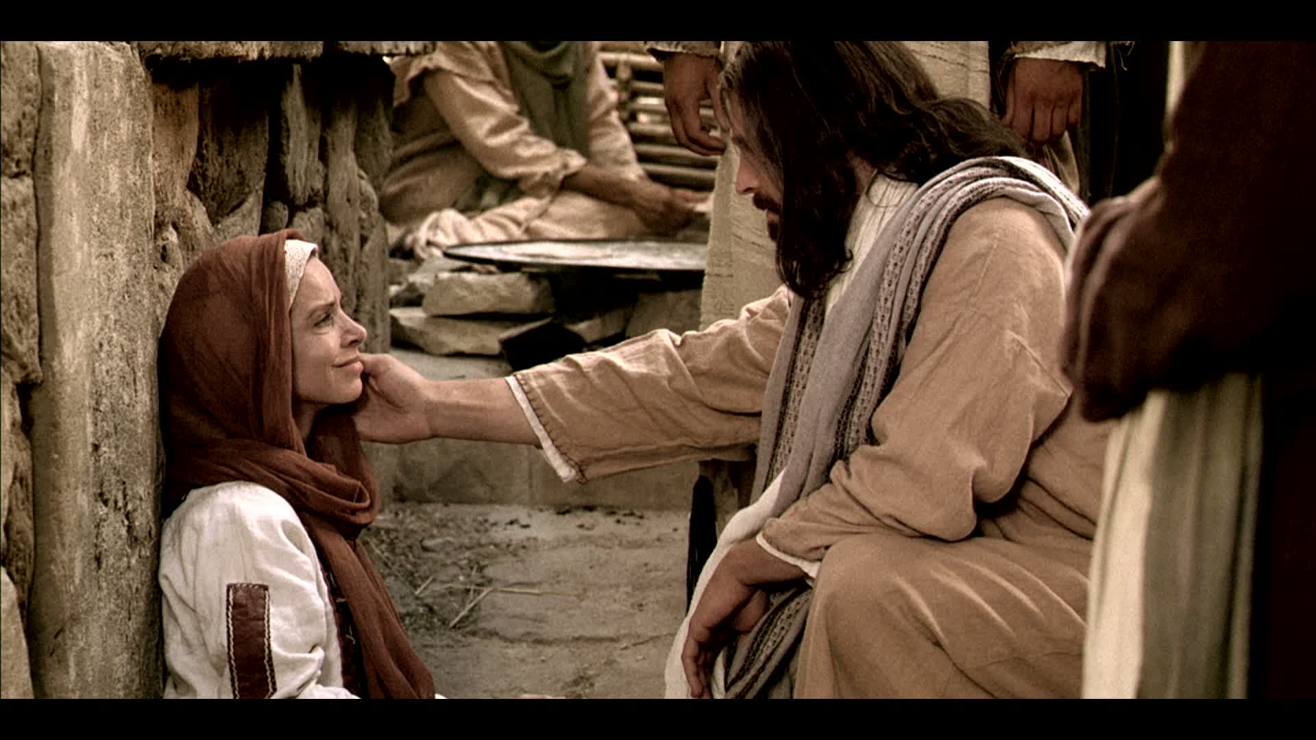 A photo of Jesus Christ kneeling before a woman sitting on the ground with his hand stretched out.