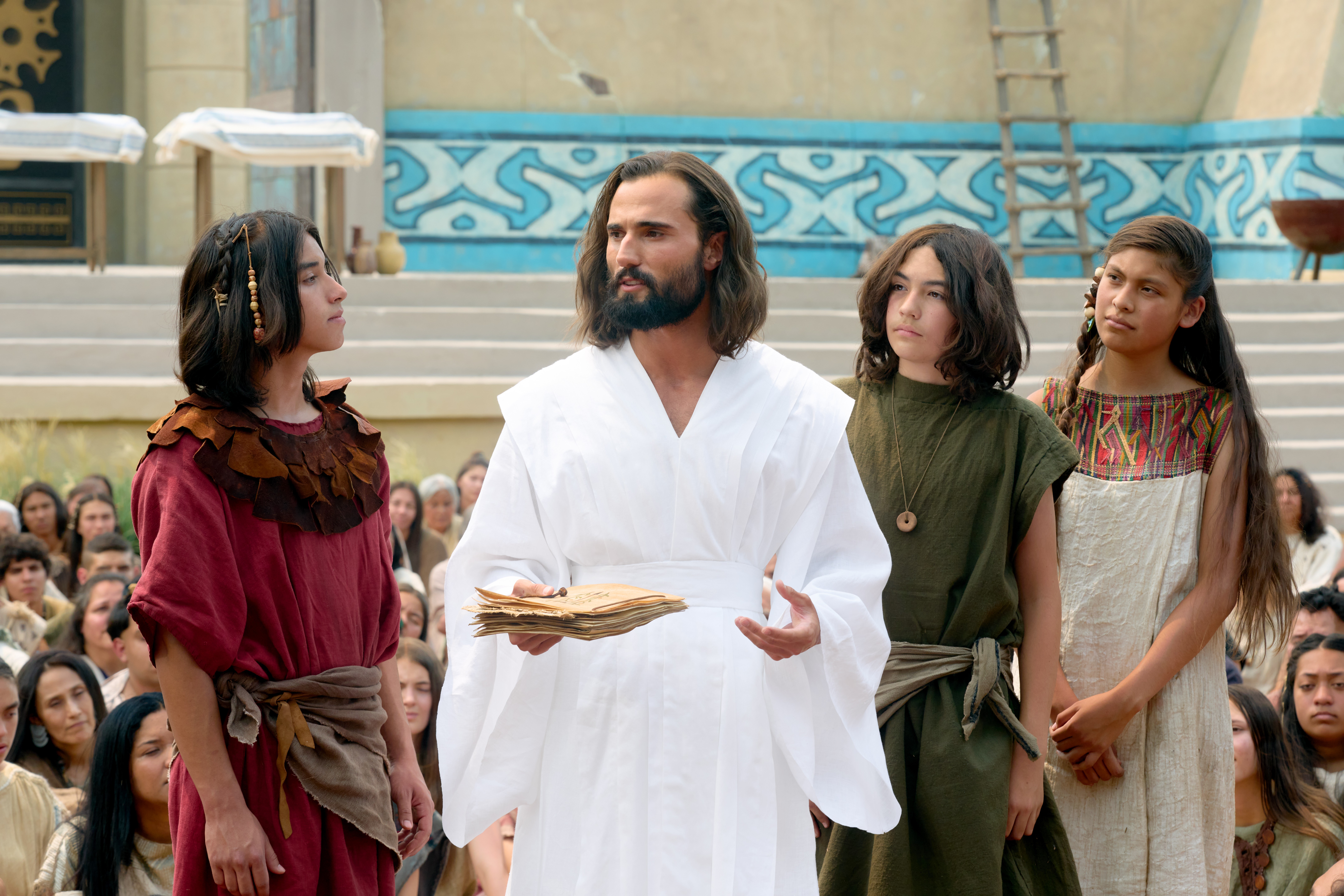 The resurrected Savior, Jesus Christ, appears to the ancient inhabitants of the Americas and teaches them his Gospel. Three youth are standing by his side as he holds writings in his hands.