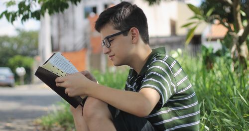 戴着眼镜的男青年，坐在户外读经文。