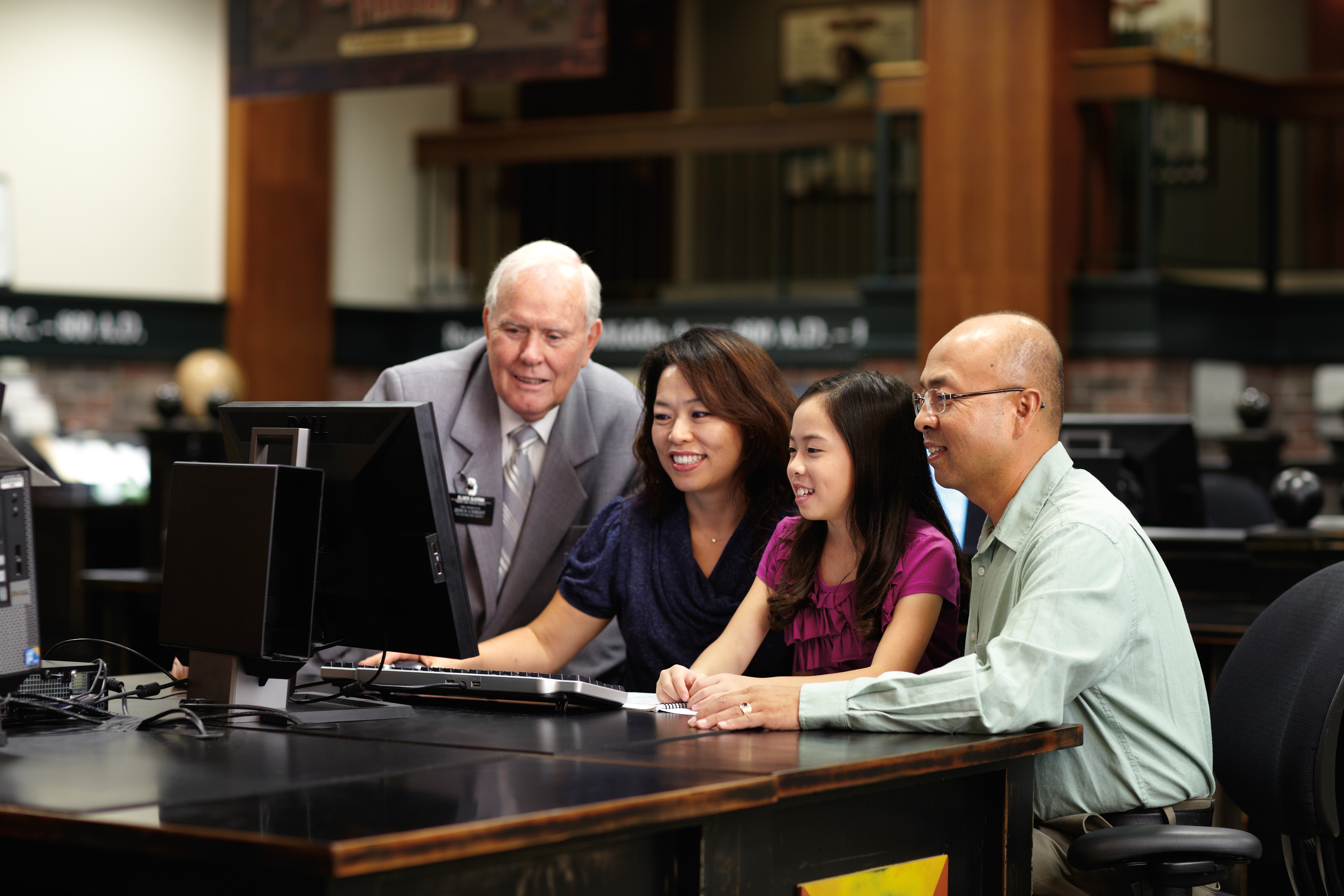 A senior elder missionary helps a young family at the computer do family history research.