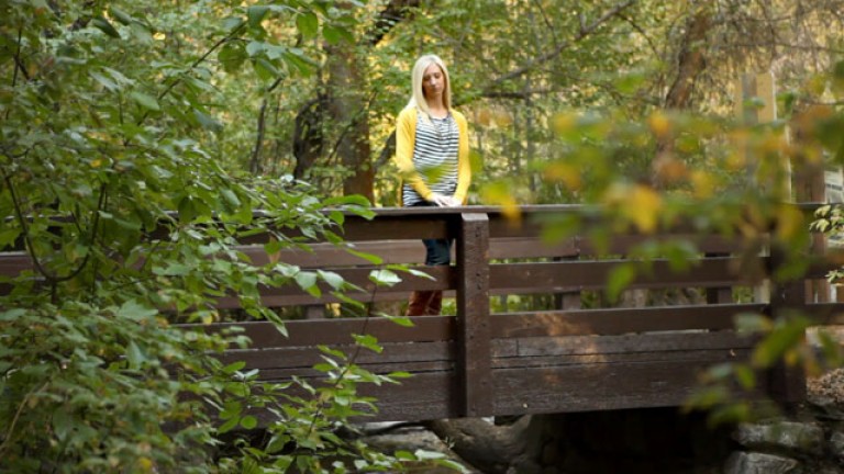A woman stands alone on a bridge in the woods