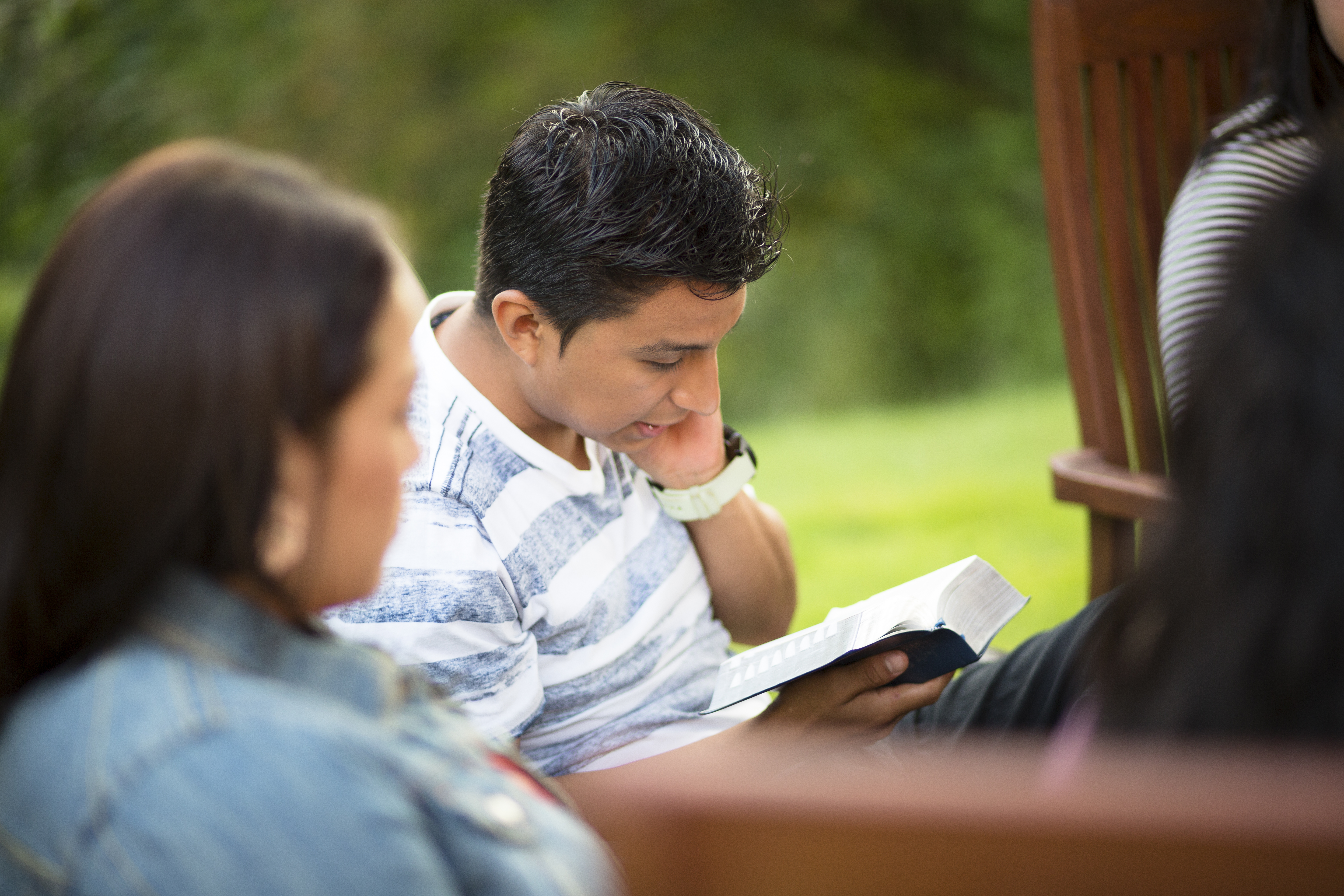 A young man reads from the scriptures while others sit around and listen.