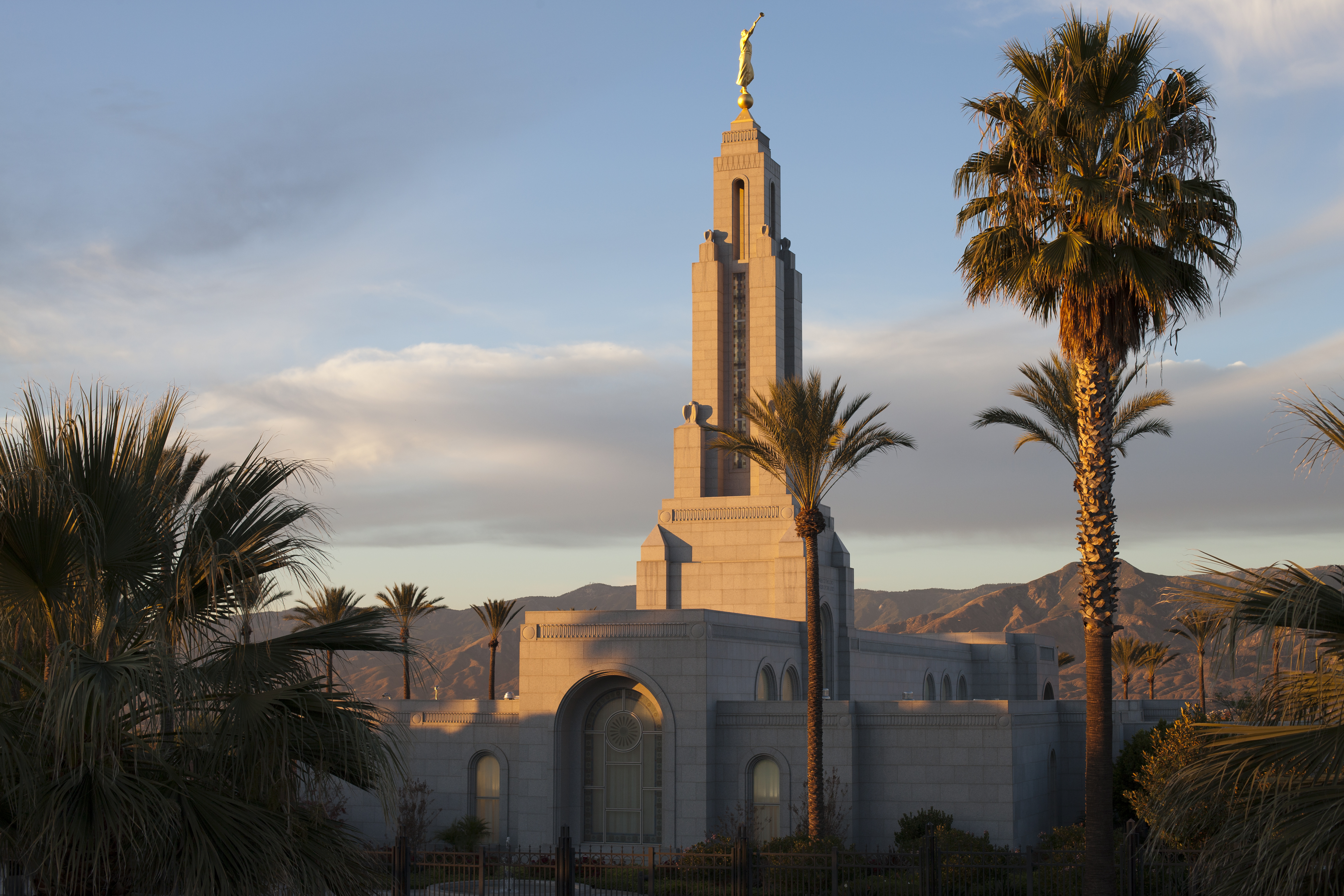 The top of the Redlands California Temple, including a view of some windows and the spire. Trees surround the temple at sunset.