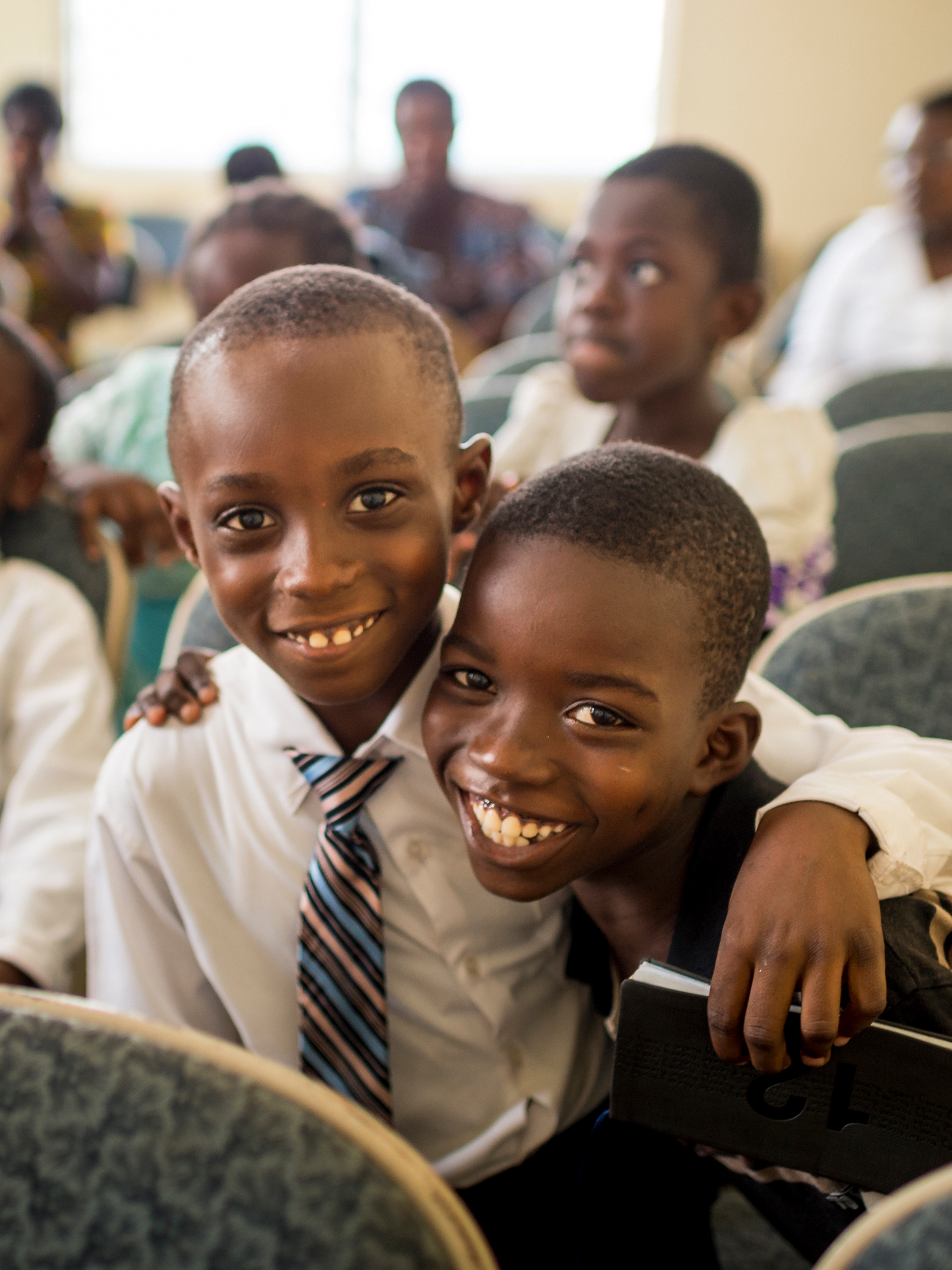 Two Primary-age boys in Ghana, smiling, with their arms wrapped around each other.