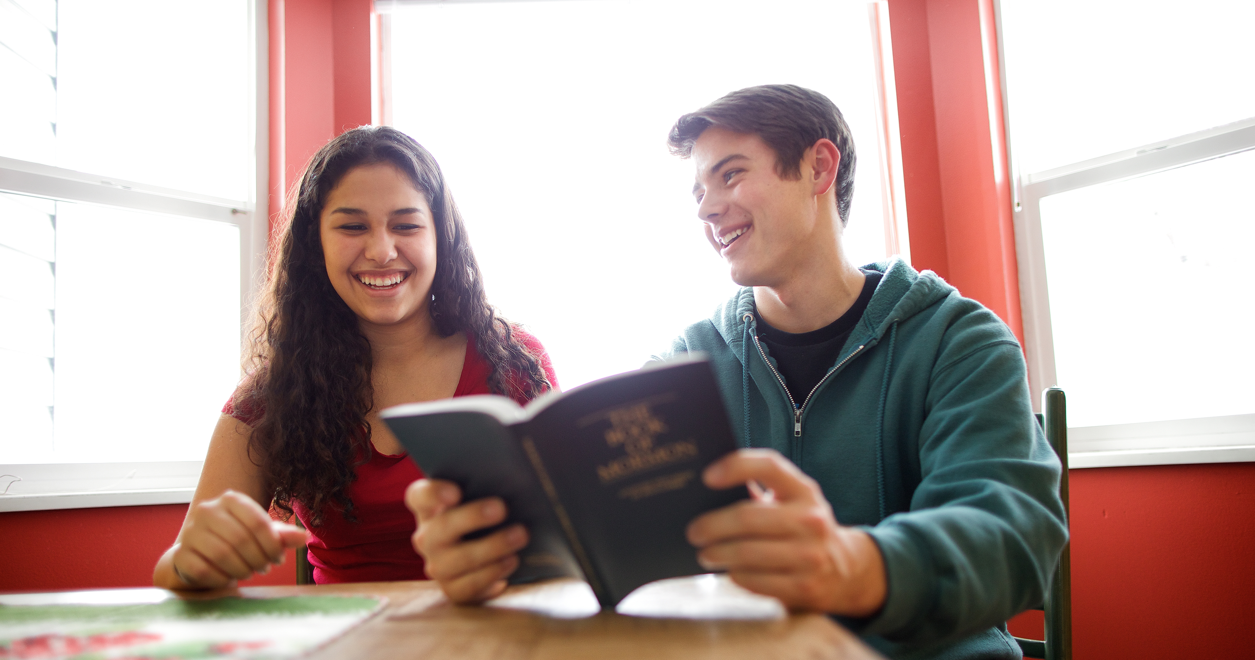 A young woman sharing a copy of the Book of Mormon with a young man.