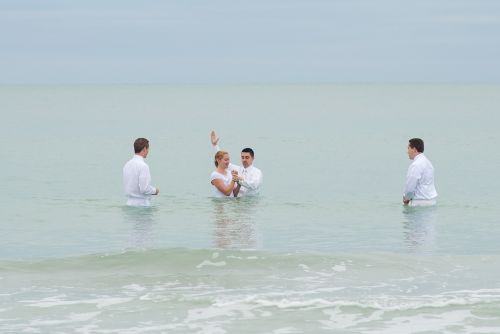 A missionary baptizing a young lady in the ocean off the coast of Florida, with two missionaries witnessing.