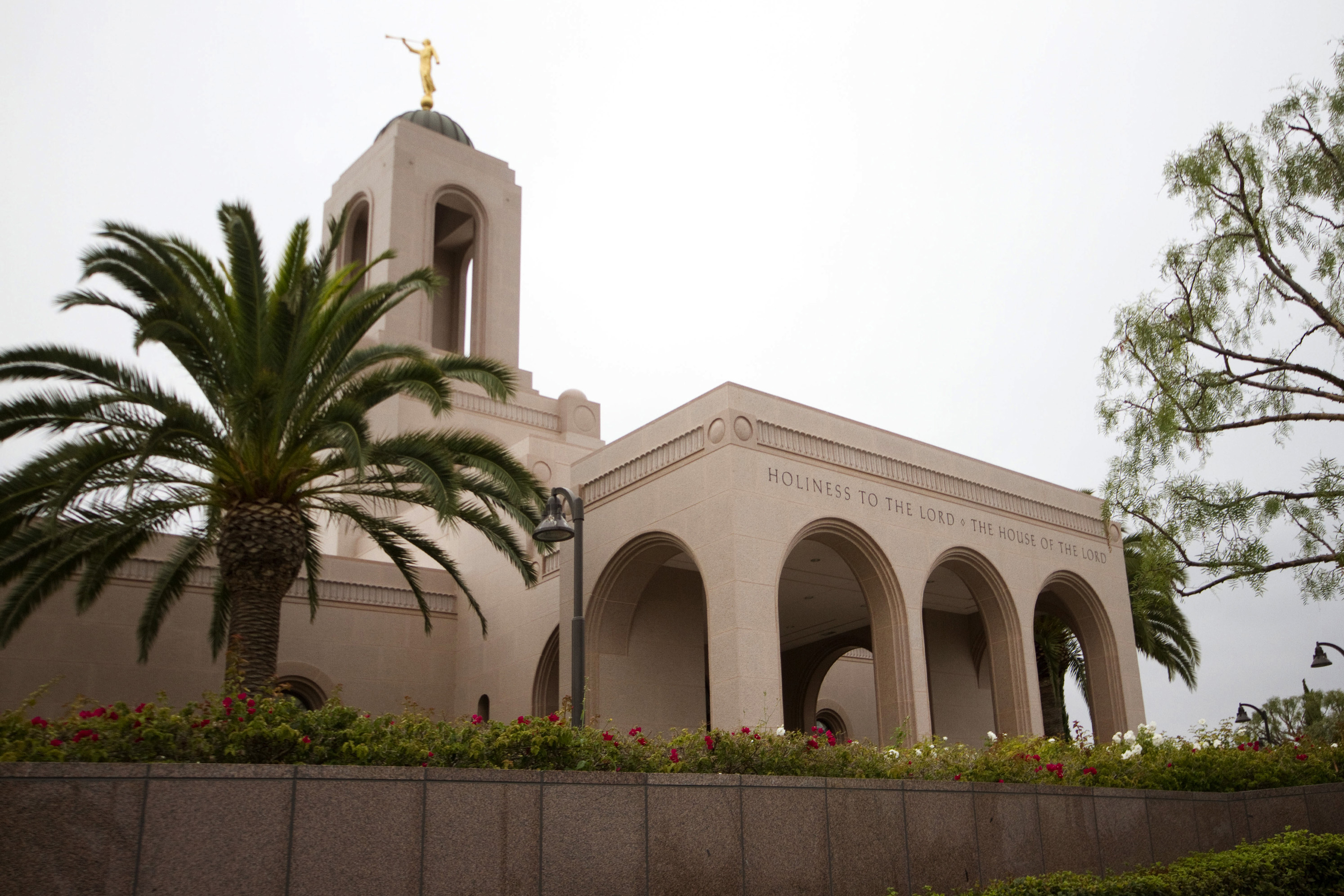 The entrance to the Newport Beach California Temple, with a nearby palm tree and the words “Holiness to the Lord: The House of the Lord” engraved over the door.