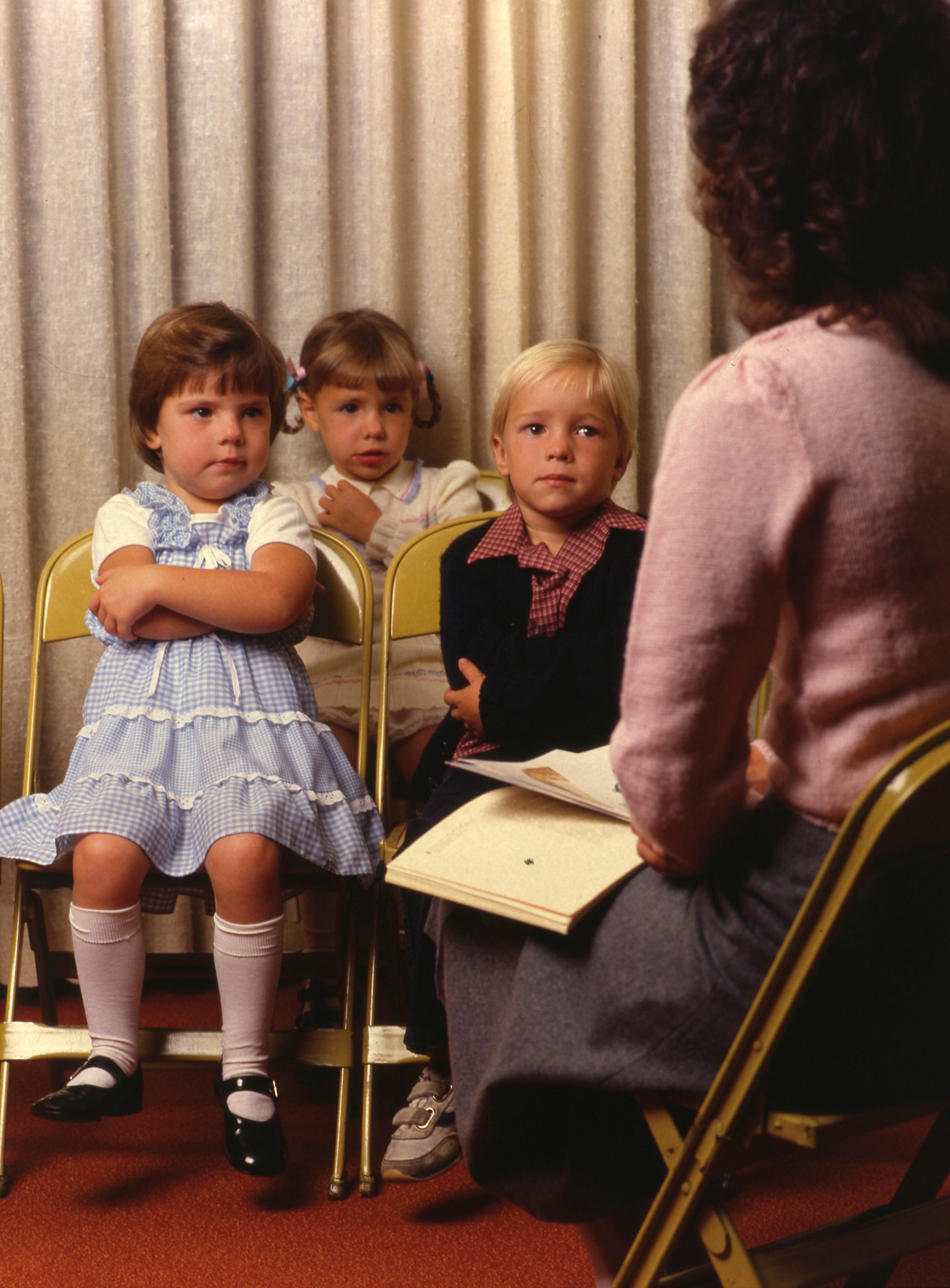 Three children sitting in a Primary class, listening to their teacher.