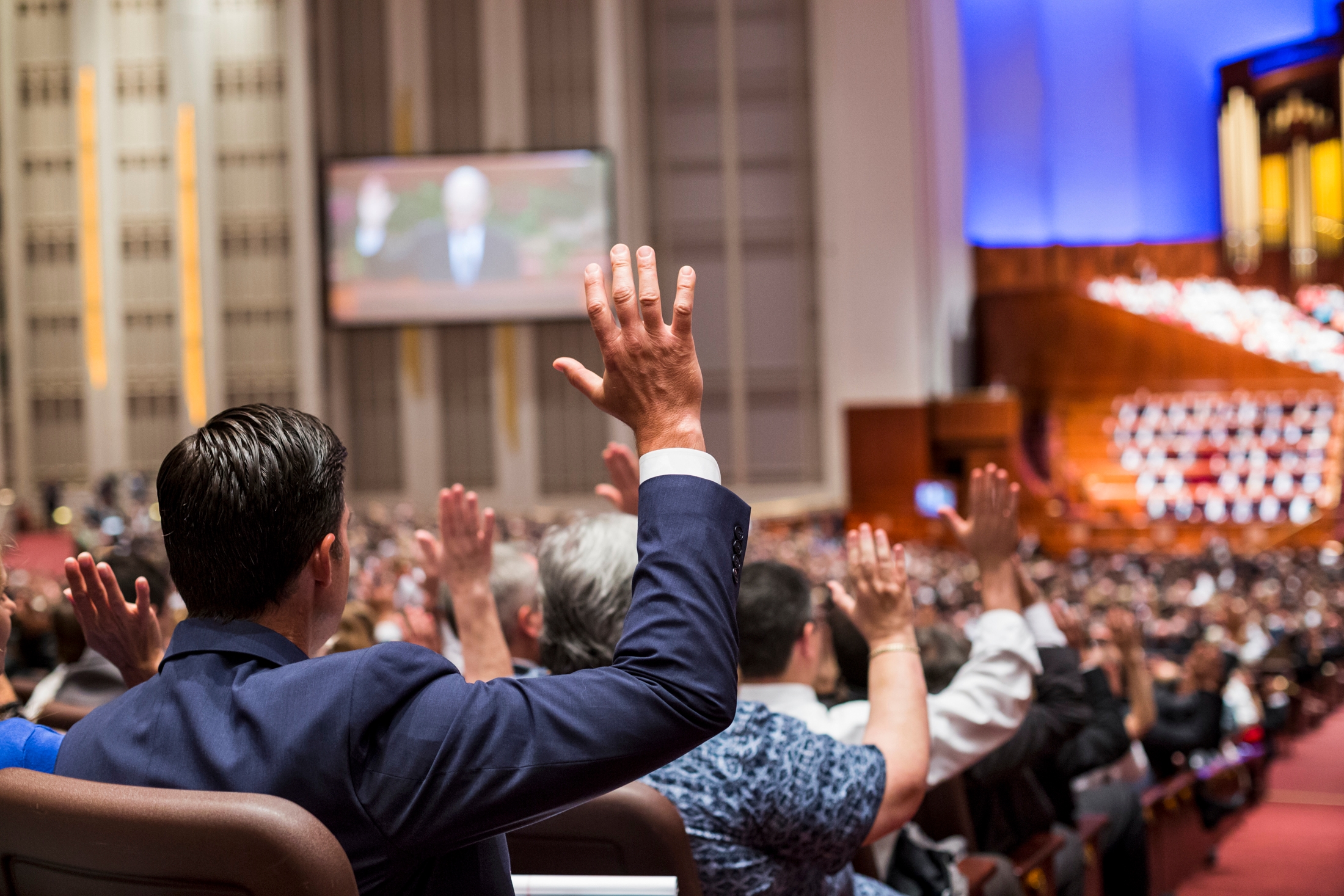 A congregation raising their hands to show a sustaining vote at general conference.