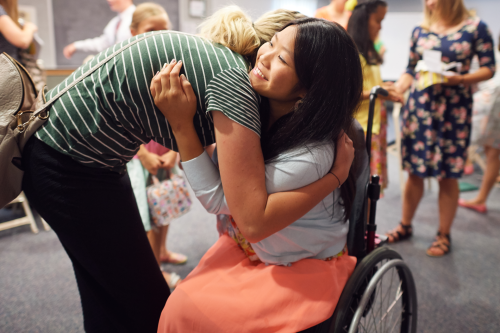 A girl in a wheelchair is talking with other young women and getting a hug