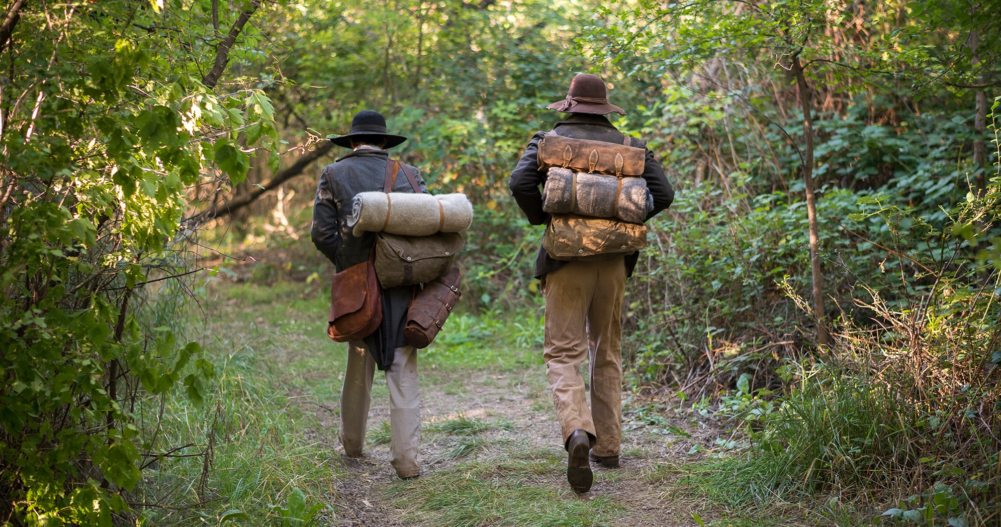 Actors portray early missionaries leaving home for their missions with supplies on their backs.