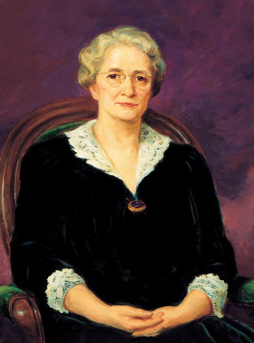 A painted portrait by Lee Greene Richards of Amy Brown Lyman against a purple background, sitting in a wooden chair with green upholstery. She is wearing a black dress trimmed in white lace.