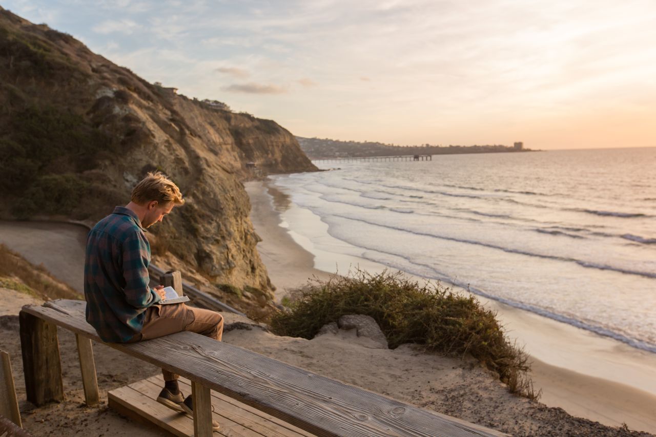 A man studies the Book of Mormon on a beach