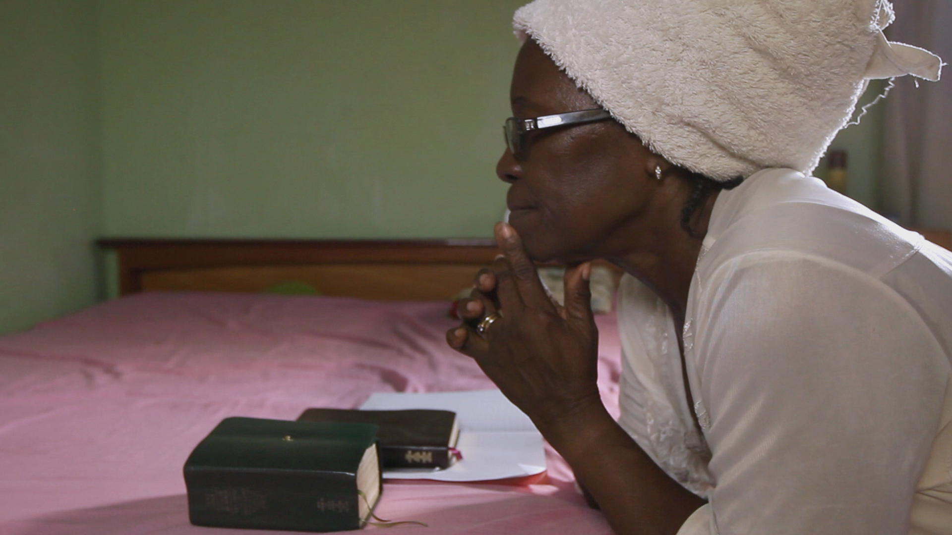 A photo of a woman kneeling by her bed with her scriptures, saying a prayer.