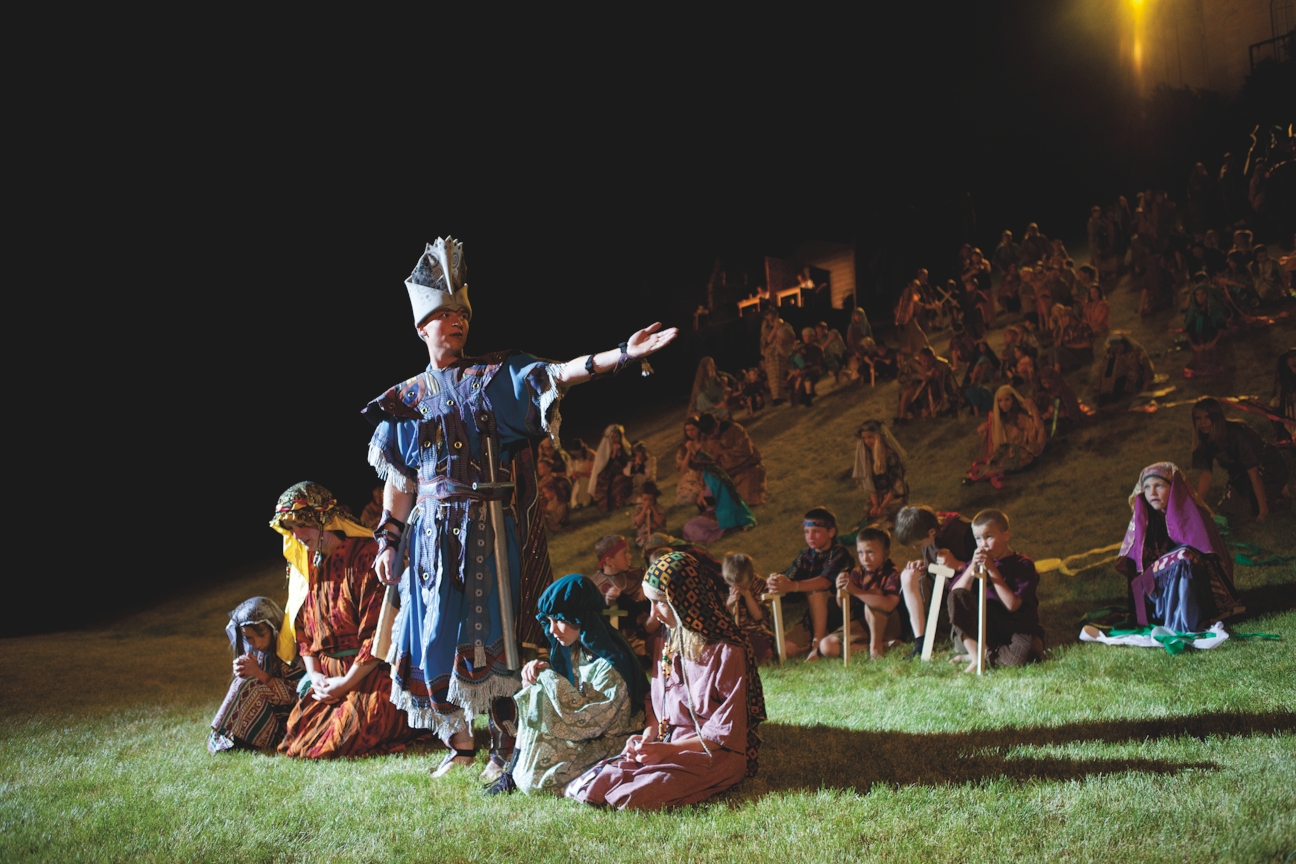 One Nephite standing with an outstretched arm in front of many Nephite children sitting down at the Manti Pageant.