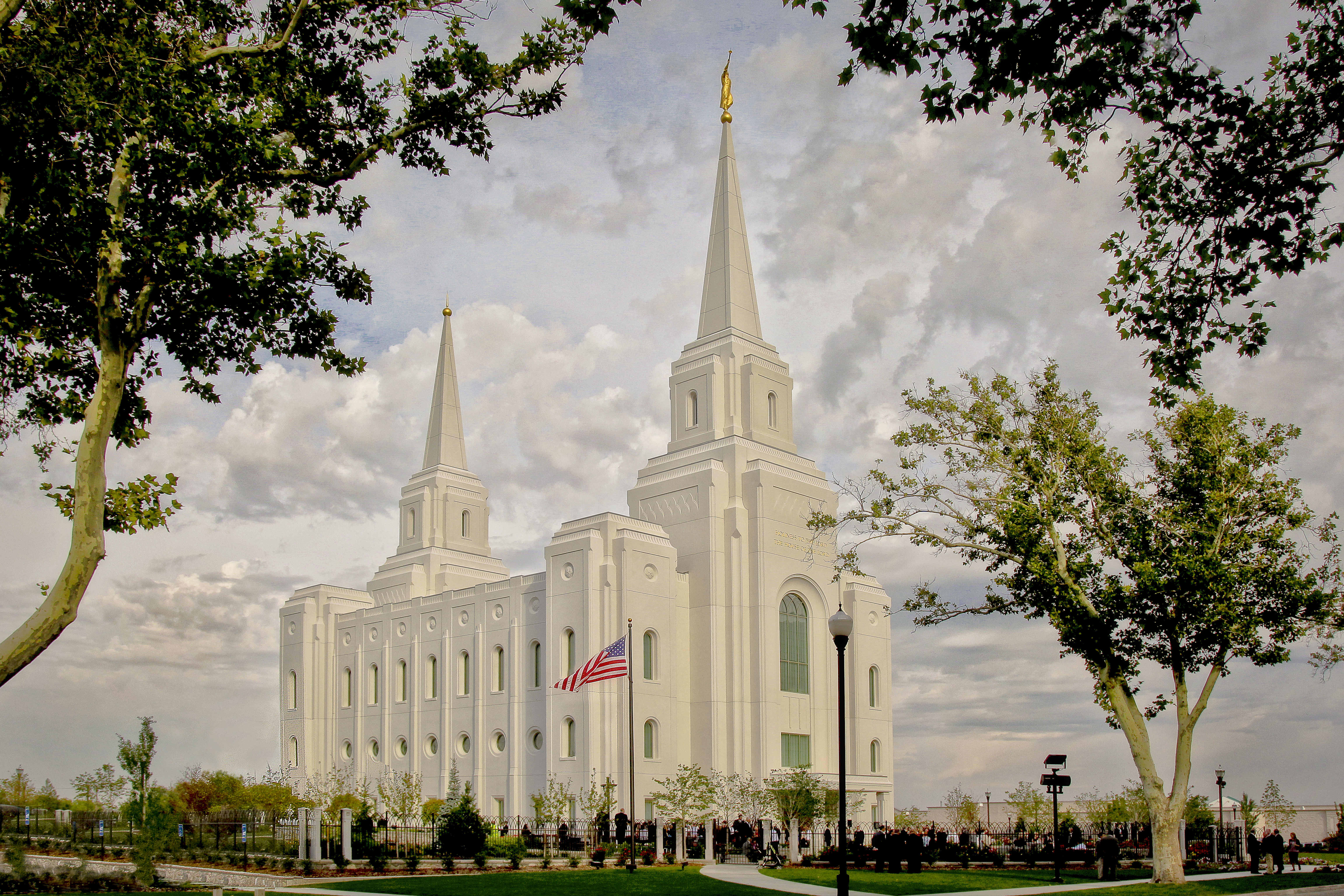 The Brigham City Utah Temple and grounds in the daytime, with green trees and an American flag in the foreground.