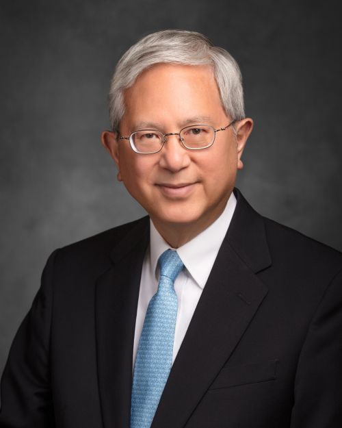 A portrait of Elder Gerrit W. Gong wearing a black suit and a red and blue striped tie.