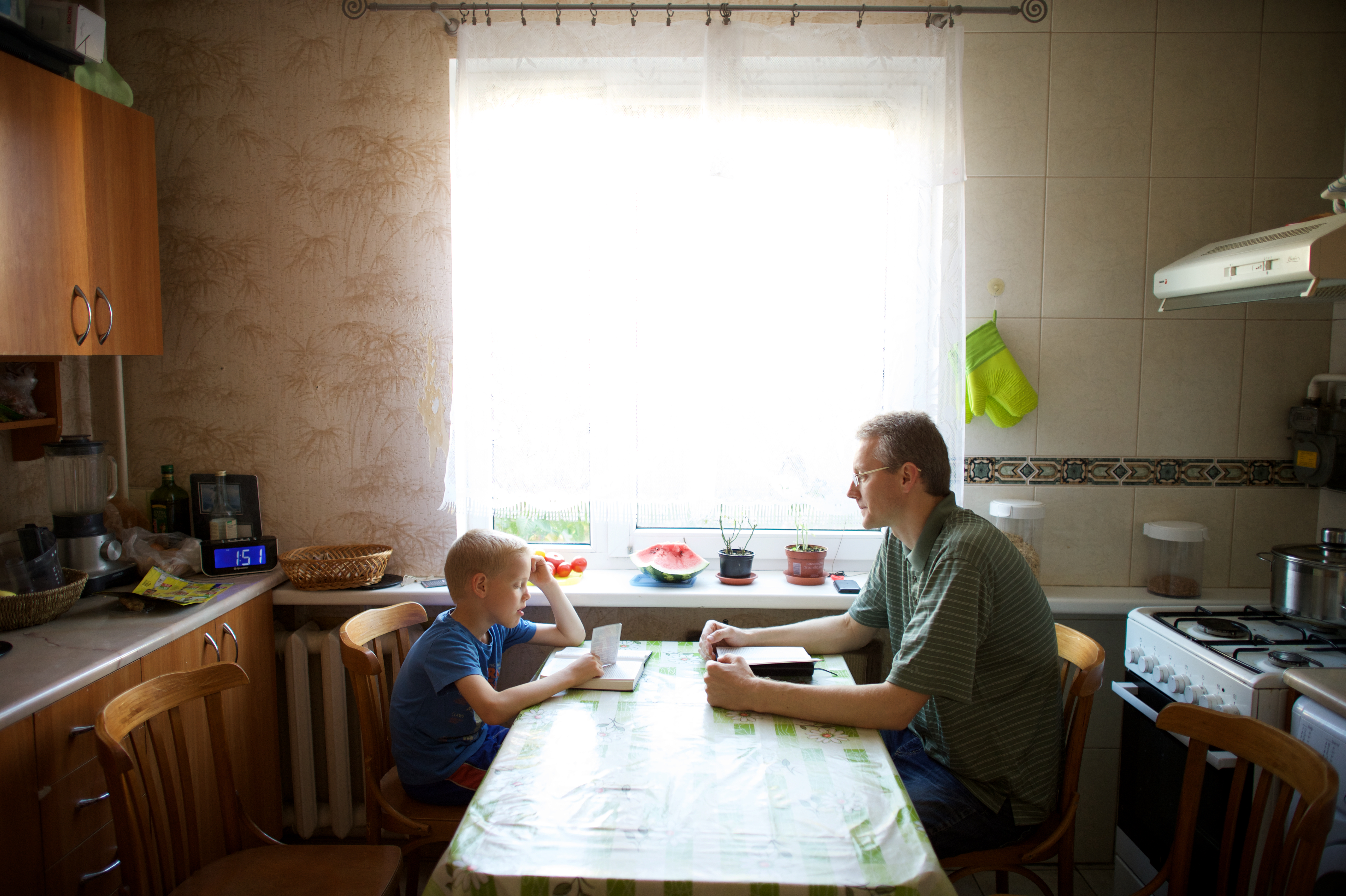 A Latvian father leads his family in scripture study at the table, his son reads.