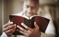 Unas manos entrelazadas reposan sobre las páginas abiertas de una Biblia