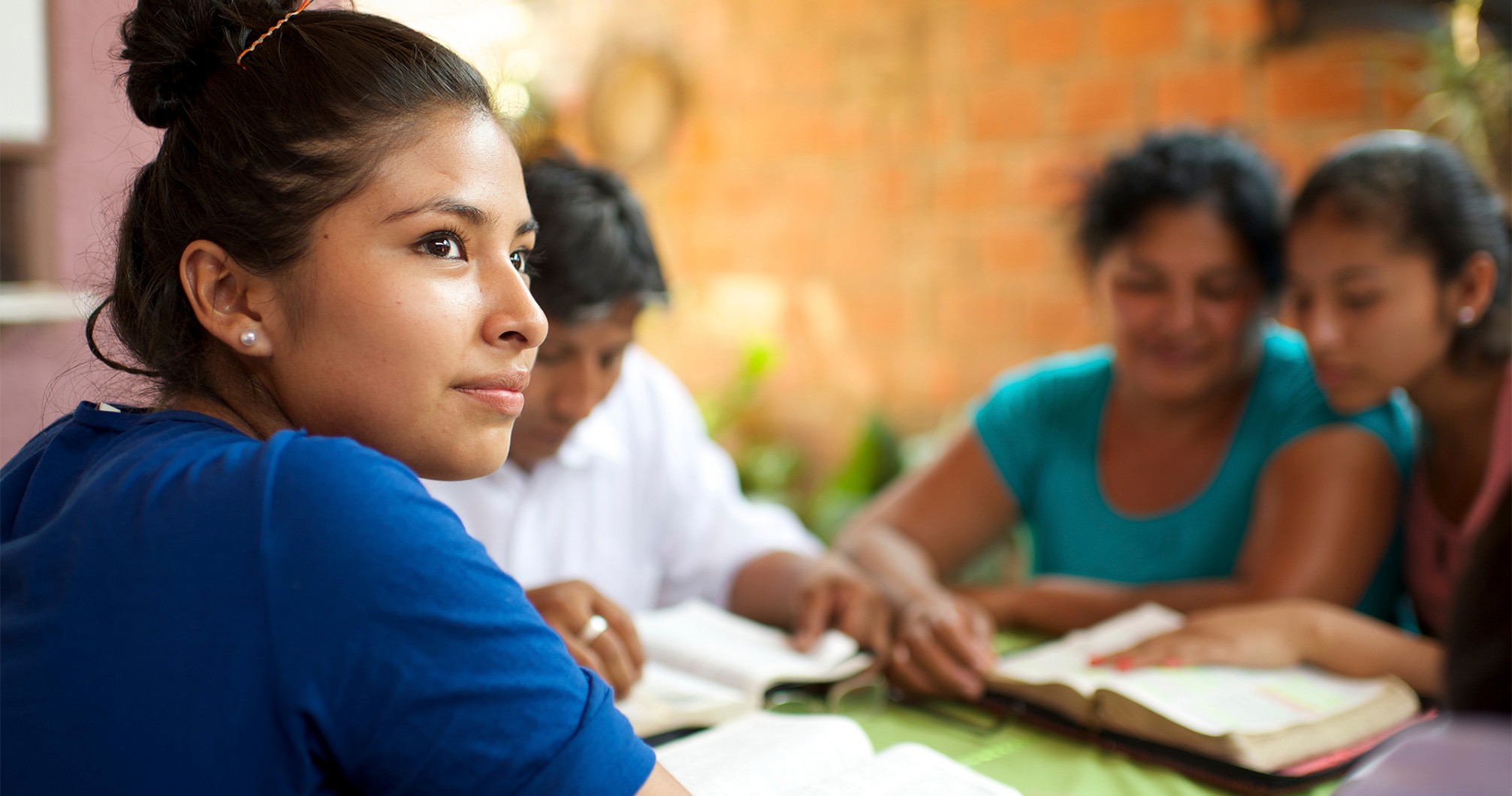 A young woman in Bolivia sitting around a table with her family reading scriptures.