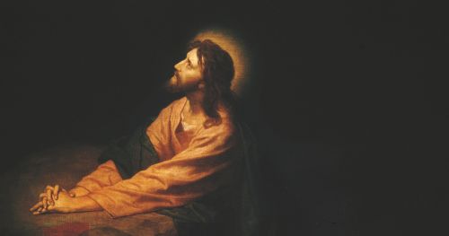 Jesus Christ kneeling as He prays and atones in the Garden of Gethsemane. Christ is depicted wearing red and blue robes. He has His hands clasped and is resting them on a large rock. A small stream of light coming through the darkened and cloudy background shines on the face of Christ. Light emanates around Christ’s head.