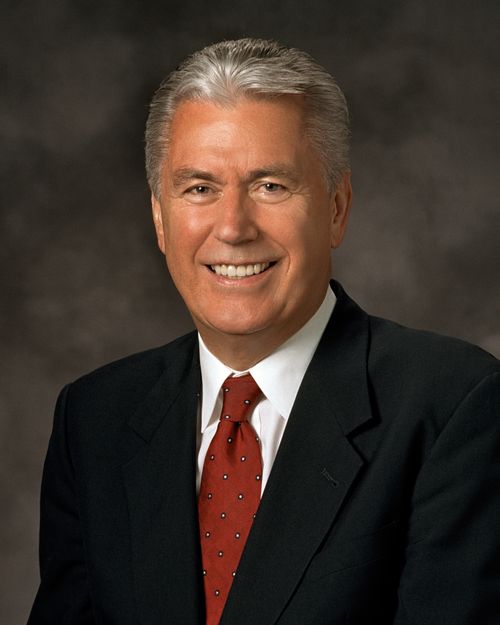 A formal portrait of President Dieter F. Uchtdorf, who is wearing a black suit and a red tie with white dots, in front of a gray background.
