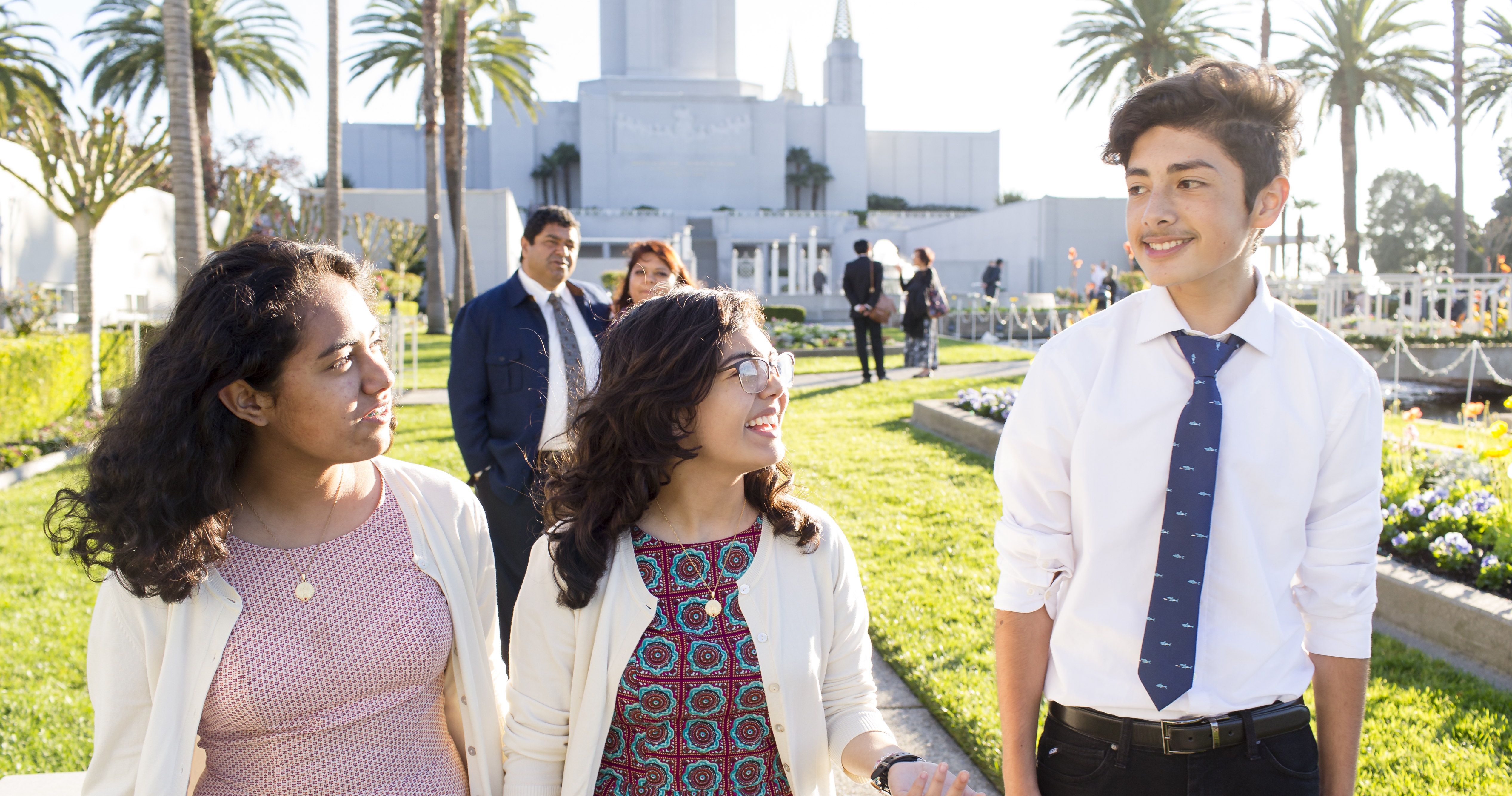 Two sisters interact with a young man while their parents watch them from behind.Photo taken on the grounds in front of the Oakland California Temple.