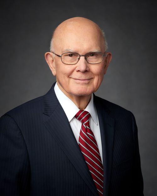 A portrait of President Dallin H. Oaks wearing a black pinstripe suit and a red and white striped tie.