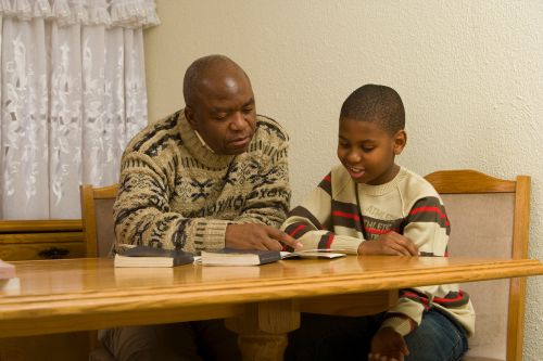 An African father and son looking at a Church publication.  The scriptures are sitting on the table in front of them.