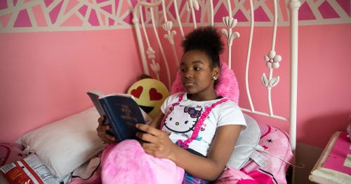 เยาวชนหญิงนั่งอ่านพระคัมภีร์อยู่ในห้องนอนของเธอ