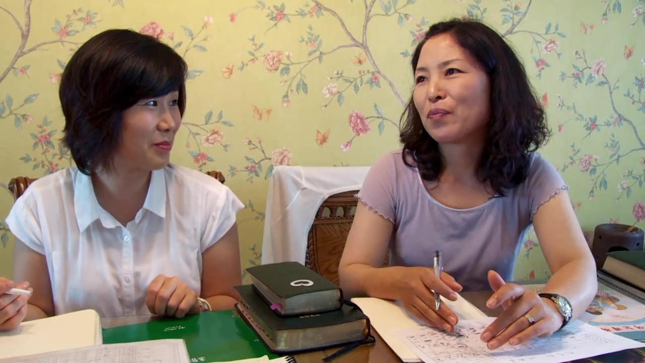 Two women sit at a table with binders and paper