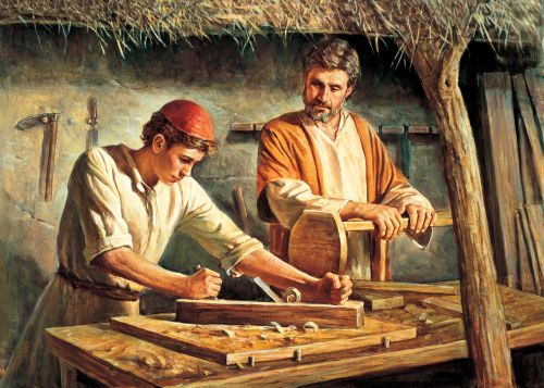 Young Jesus standing next to Joseph in the carpenter’s shop, working with tools on the wood while Joseph supervises.