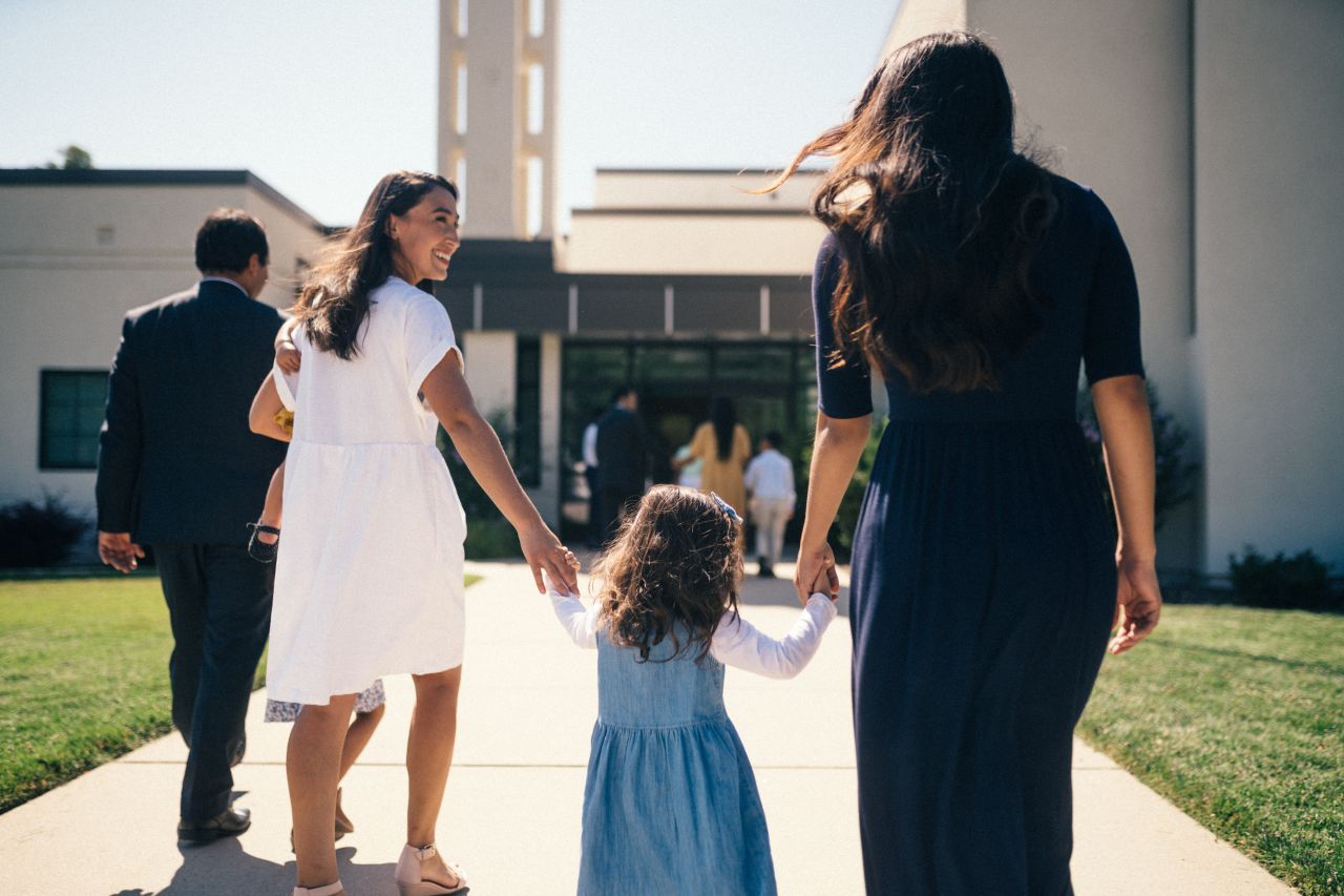 Una niña pequeña toma la mano de una mujer cuando entran al centro de reuniones de una iglesia