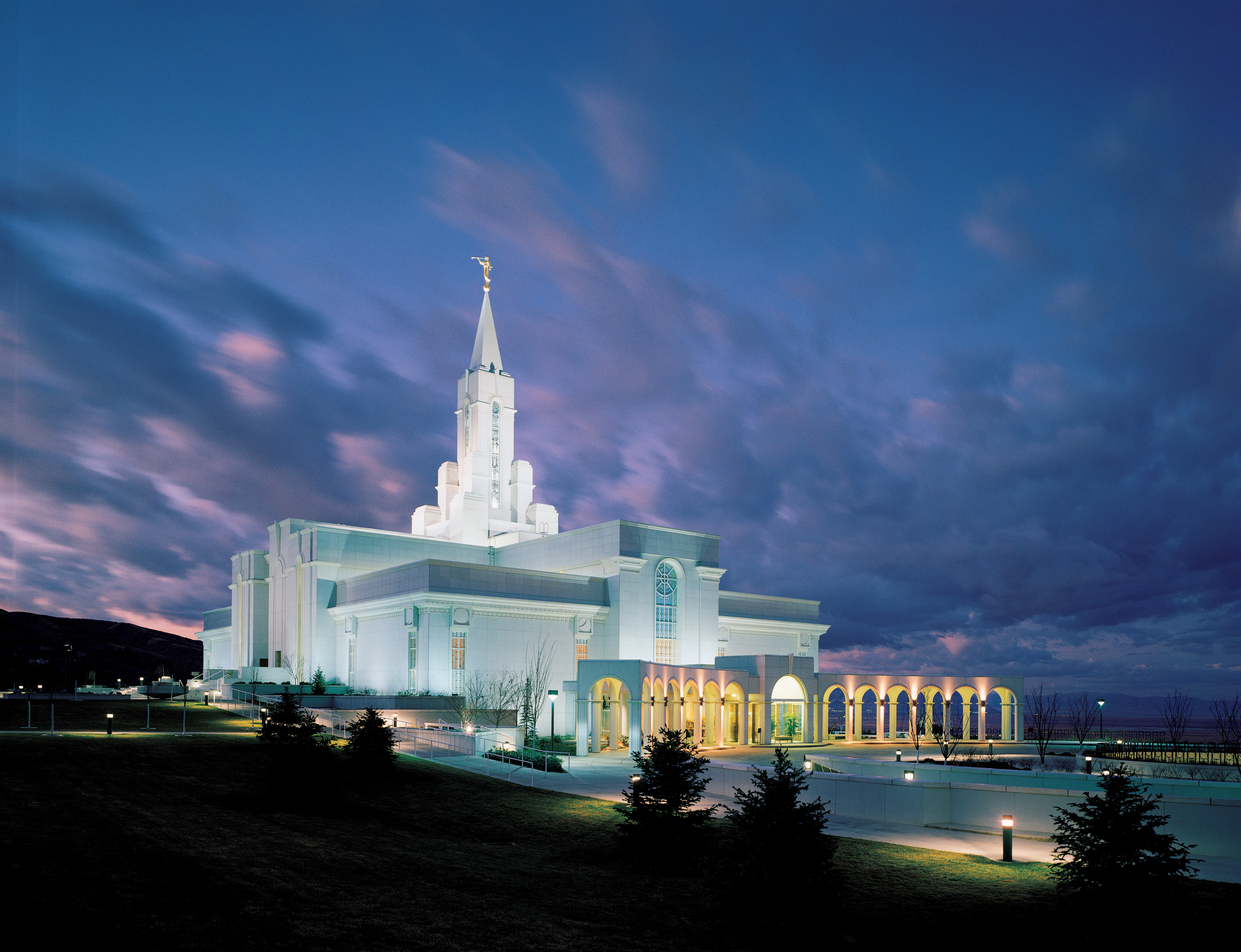 The Bountiful Utah Temple lit up in the evening, with clouds in the sky.