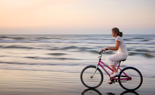Woman riding a bicycle on a beach.