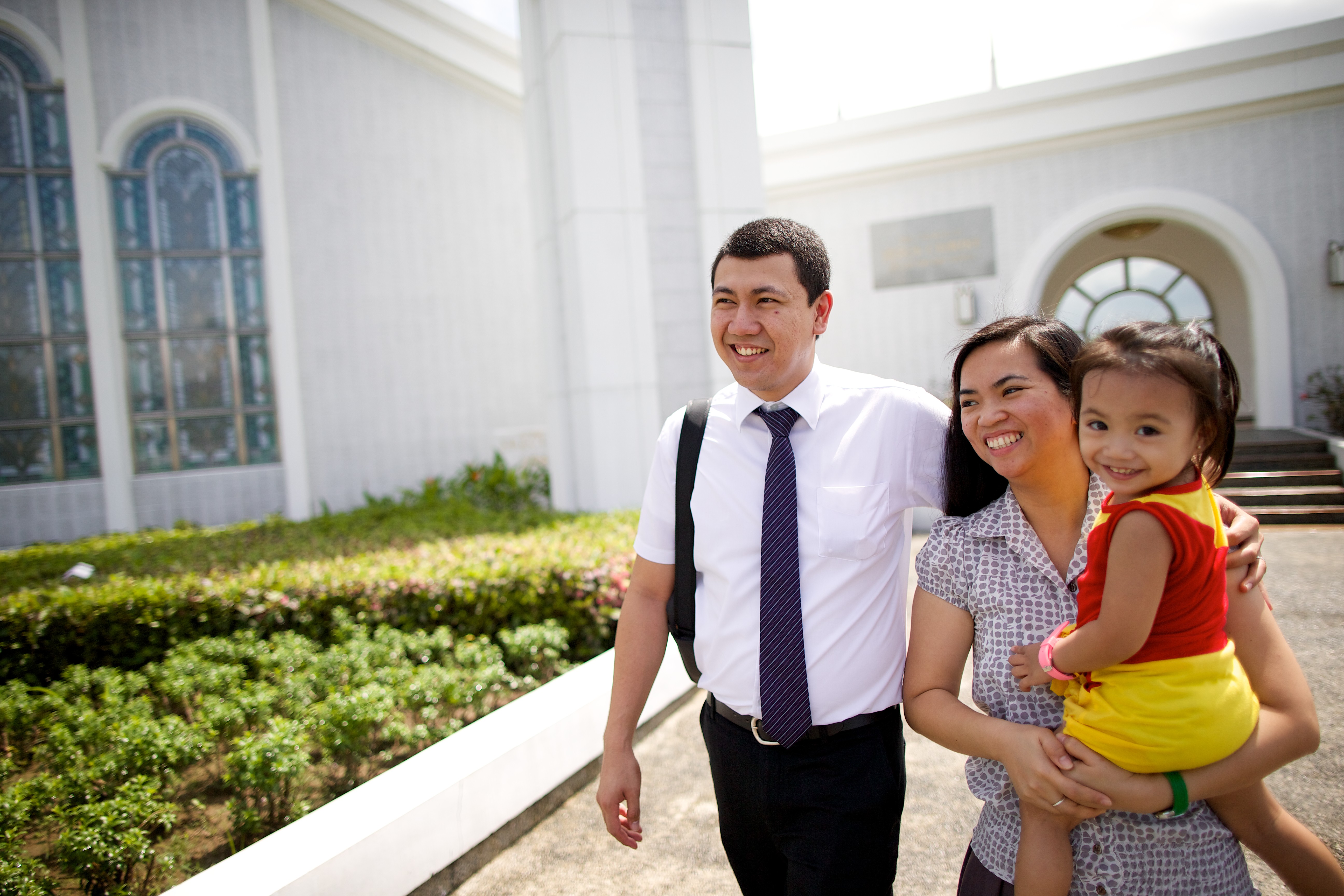 A man putting an arm around his wife’s shoulders as she carries their young daughter outside the Manila Philippines Temple.